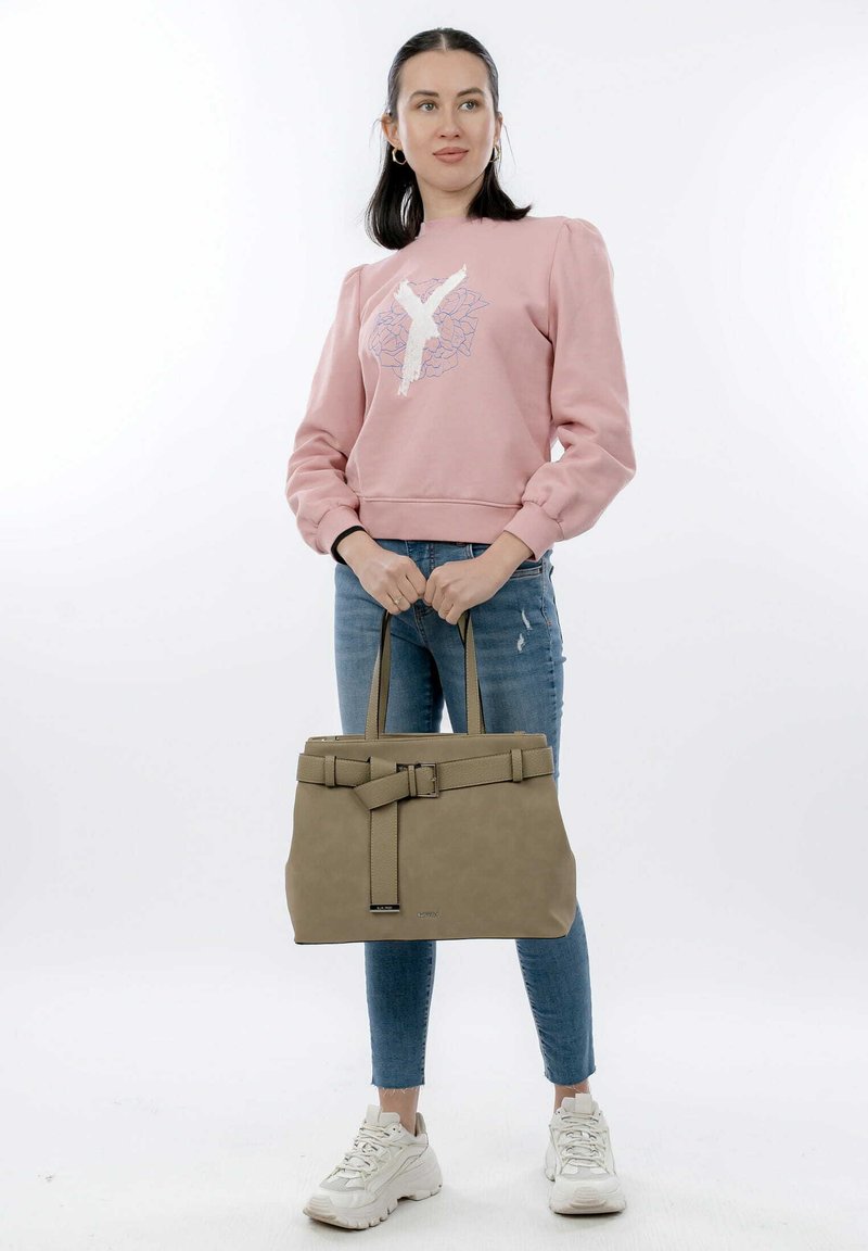 Sweatshirt rosa chiaro con maniche a sbuffo e design di lettere bianche, abbinato a jeans slim-fit blu e borsa beige con dettagli in cintura.