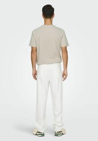 Camiseta de algodón beige, de mangas cortas, corte relajado. Pantalones de denim blancos, de pierna recta, diseño de cinco bolsillos, combinados con zapatillas ligeras.