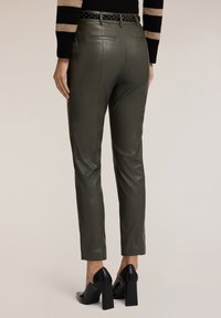 Oliwkowe spodnie z sztucznej skóry o slim fit, z tylnymi kieszeniami i czarnym, ćwiekowanym paskiem. Noszone z czarnymi, blokowymi obcasami.