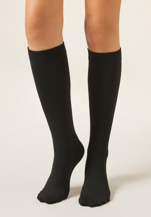 Calcetines negros hasta la rodilla hechos de tela lisa, con diseño ajustado y puños acanalados, que llegan justo debajo de la rodilla.