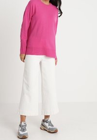 Fuchsia långärmad tröja, vita vida byxor och grå sneakers. Outfiten har en avslappnad passform med ribbade detaljer.