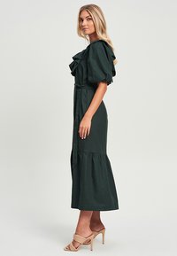 Tamnozeleni midi haljina s naboranim kratkim rukavima, pojasom u struku i lepršavom suknjom. Glatka tekstura tkanine, elegantan dizajn.