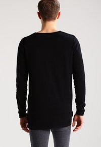 Svart långärmad tröja med rund hals, tillverkad av ett mjukt tyg, med rak skärning och sidofickor vid fållen.