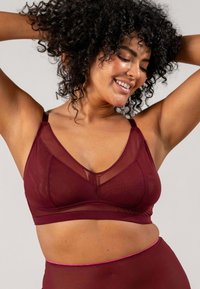 Burgundyröd bralette med V-ringning; har genomskinliga nätpaneler och mjukt material. Justerbara remmar med minimalistiska sömmar.