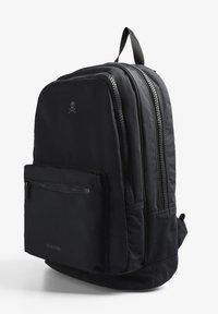 Mochila negra de nailon con dos compartimentos con cremallera, bolsillo frontal con cremallera y un sutil logotipo de calavera en la parte delantera.