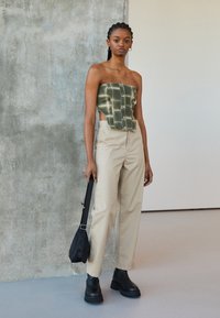 Haut croppé à carreaux verts stylé avec un devant à boutons, associé à un pantalon beige taille haute et des bottines noires chunky, tenant un petit sac.