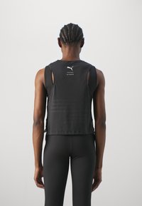 Top atletico nero senza maniche con dettagli in rete, logo sul retro e vestibilità rilassata. Abbinato a leggings neri aderenti.