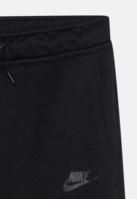 Svarta Nike-joggers med dragsko i midjan, sidofickor, en mjuk textur och en diskret logotyp i en mörkare nyans.