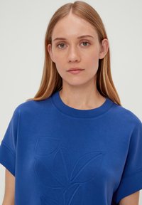 Blauwe sweatshirt met korte mouwen en een gestructureerd bloemenpatroon aan de voorkant. Ronde halslijn en zachte stof, met een relaxte pasvorm.