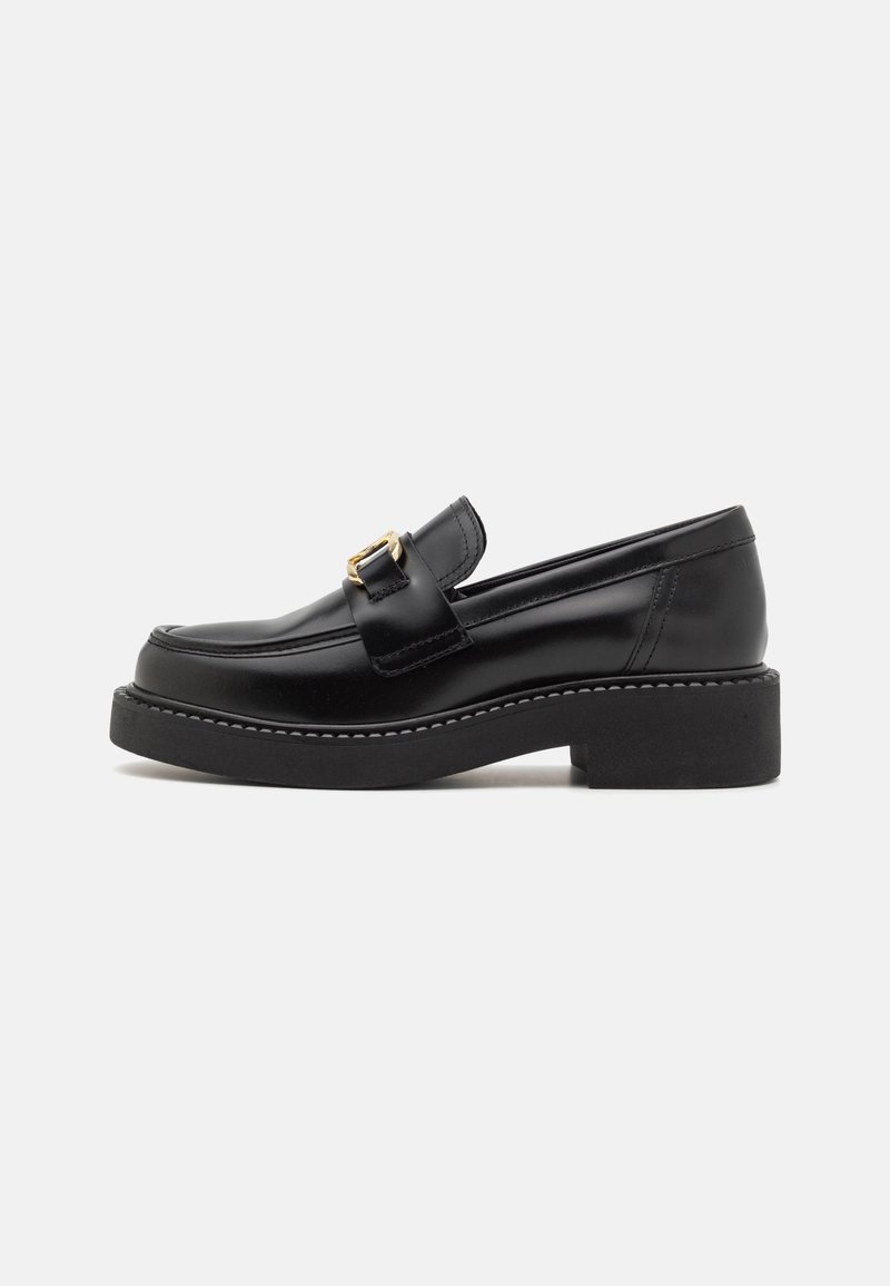 Mocassin en cuir noir avec un petit talon carré, un bout arrondi et une boucle dorée décorant la lanière avant.