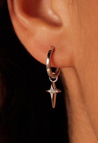 Boucle d'oreille en argent avec une étoile pendante ornée d'un petit accent en diamant, présentant une finition poli et une texture lisse.