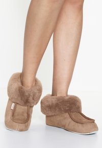 Brown suede slippers with a faux fur cuff, round toe design, and a soft texture. The sole is white, contrasting with the upper material.