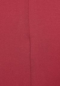 Gebreide stof in een diepe rode kleur met fijne ribbels en een zichtbare verticale naad aan één kant.