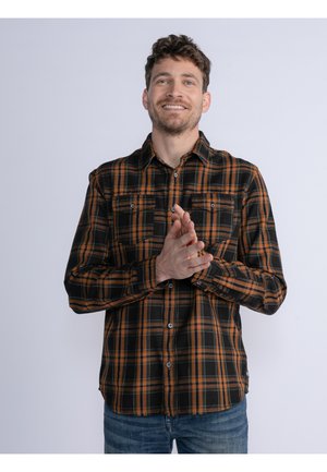 Camisa de cuadros negra y naranja de mangas largas con dos bolsillos en el pecho, cierre de botones en la parte delantera y cuello, llevada sobre unos pantalones vaqueros azules.