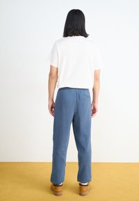 Pantalon en coton bleu avec une coupe décontractée, taille élastique et poche arrière décorative, associé à un t-shirt blanc uni.