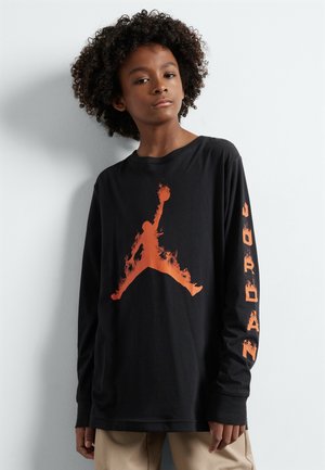 Camiseta de manga larga negra con un gran logo de Jumpman con patrón de llamas naranjas en el frontal y la palabra "JORDAN" impresa en naranja a lo largo de la manga.