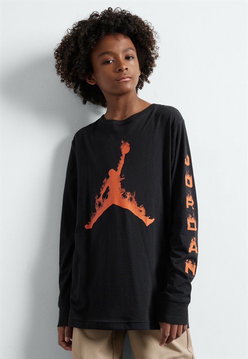 Camiseta de manga larga negra con un gran logo de Jumpman con patrón de llamas naranjas en el frontal y la palabra "JORDAN" impresa en naranja a lo largo de la manga.