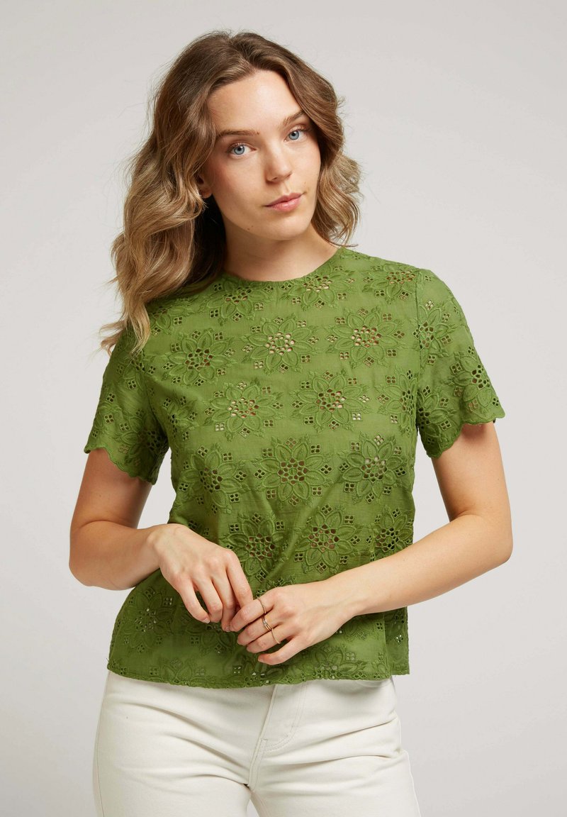 Blouse verte brodée avec motif en dentelle florale, manches courtes à volants et col rond, fabriquée en tissu léger.