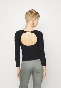 Musthave mustaga pikkade varrukatega topp, millel on seljaosas kaarjas lõige, mis rõhutab talje kuju ja on pehmest materjalist. Kombineeritud heledate hallide pükstega.