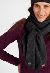 Bufanda gris oscuro hecha de una tela suave, drapeada de manera suelta con un nudo. Llevada con una blusa texturizada de color p úrpura; logotipos de la marca visibles en colores contrastantes.