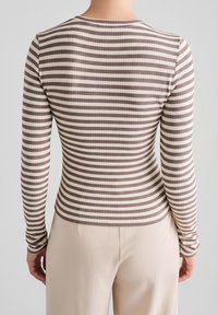 Osoba ubrana w dopasowaną bluzkę z długim rękawem w poziome brązowo-białe paski, zestawioną z jasnobeżowymi spodniami, pokazana od tyłu.