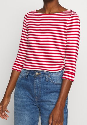 Person iført rød og hvid vandret striped trekvartærms-top med højtaljede blå denimjeans.