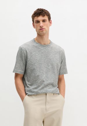 Gray and white striped short-sleeve t-shirt with a crew neckline, made of a soft fabric, paired with beige trousers.