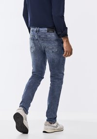 Herrblå denimjeans med slim fit, femfickorsdesign, urtvättad tvätt och en svart varumärkesetikett på den bakre midjebanden.