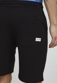 Shorts negri din bumbac, cu o croială relaxată, având un buzunar la spate și un mic eticheta de marcă. Elasticul de la talie este striat.