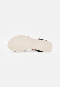 Sandale noire avec une semelle plate striée et des accents en cuir beige. Équipée de sangles réglables et d'une semelle intérieure texturée.