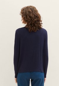 Granatowy top z długim rękawem i okrągłym dekoltem, wykonany z miękkiego materiału, charakteryzuje się luźnym krojem i bocznymi rozcięciami u dołu, co zapewnia swobodę ruchów.