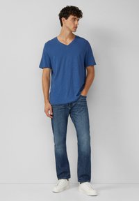Blauwe v-hals t-shirt met korte mouwen, gemaakt van zachte stof. Draagt samen met recht-toe-rechtaan jeans en witte sneakers. Eenvoudige, casual outfit.