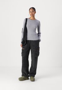 Haut à manches longues côtelé gris associé à un pantalon cargo noir duveteux avec poches et accents marron ; des chaussures à plateforme vertes complètent l'ensemble.