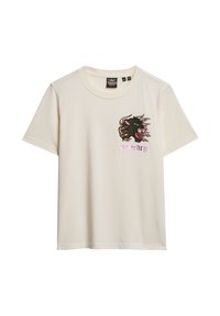 T-shirt en coton crème avec des manches courtes. Présente un graphique brodé noir et rouge d'un chat sauvage avec le texte rose "urgence" en dessous.