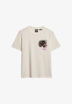 Krømfarvet bomulds t-shirt med korte ærmer. Har et broderet grafik af en vild kat i sort og rødt med pink tekst "nødsituation" nedenfor.
