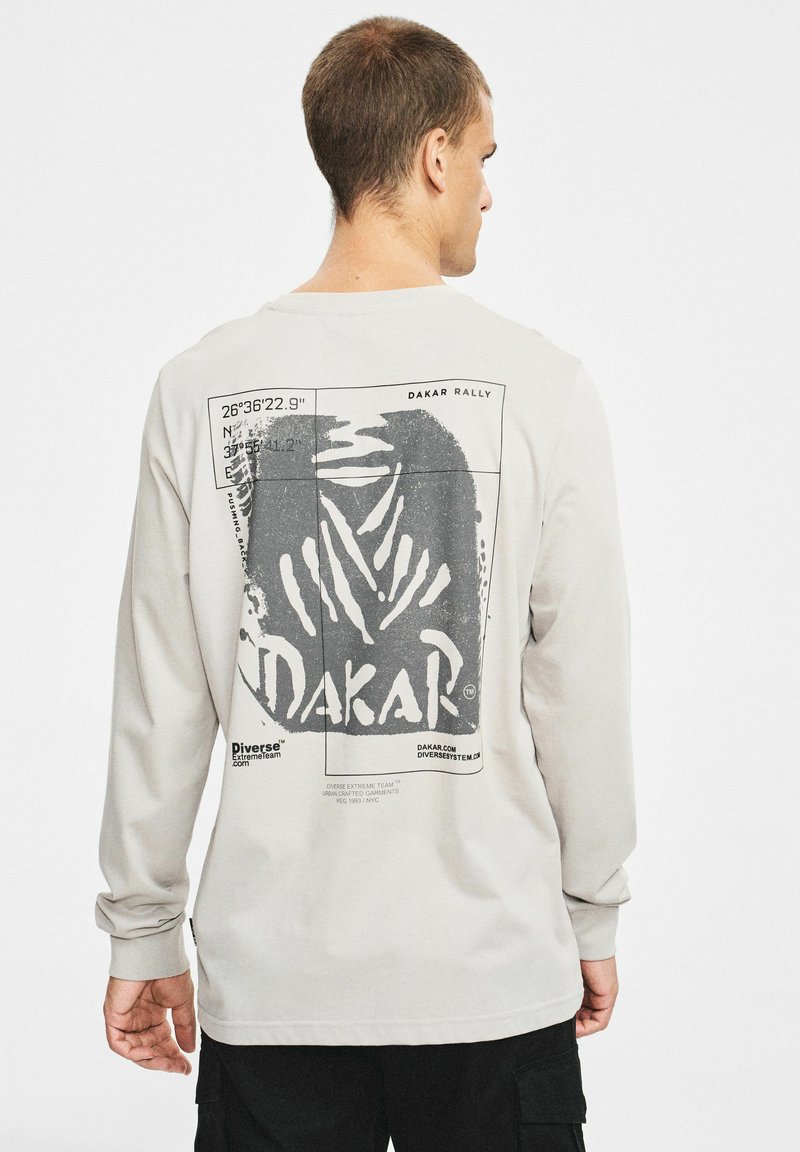 Szara koszulka z długim rękawem z czarnym grafiką Dakar Rally na plecach, w układzie prostokątnym z tekstowymi detalami.