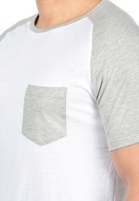 Short-sleeve T-shirt with a white body and light gray raglan sleeves. Features a left chest pocket with matching gray fabric. Smooth texture.