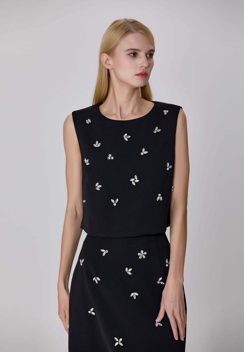 Top sans manches noir avec un col rond, orné de décorations florales en argent, fabriqué à partir d'un tissu lisse.
