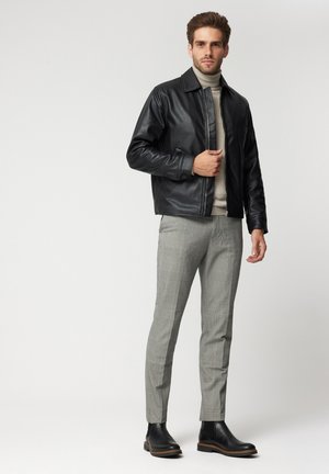 Czarna skórzana kurtka z kołnierzem, w zestawieniu z jasnoszarym golfem, szarymi spodniami w kratę i czarnymi botkami na kostkę.