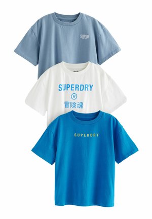 Drei T-Shirts ausgestellt: eines hellblau, eines weiß mit blauer Grafikschrift und eines leuchtend blau mit gelber Schrift. Aus Baumwollstoff, mit Rundhalsausschnitt.