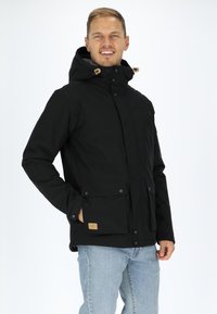 Black jacket with a hood, featuring snap closures, two front pockets, and a textured inner lining. A tan label is visible on the left pocket.