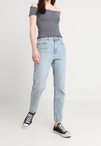 Pruhovaný top bez ramínek s volánkovými okraji, světle modré džíny s vysokým pasem a černé tenisky s bílými podrážkami. Neformální outfit.