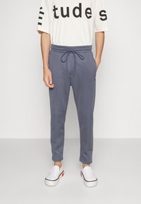 Gray cotton joggers with elastic waistband and drawstring, featuring side pockets and tapered legs, paired with white slip-on shoes.