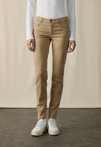 Beiga bomullbyxor med en figursydd design, framfickor och knappstängning, i kombination med vita sneakers för en avslappnad stil.