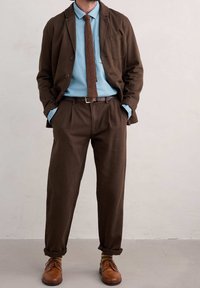 Brązowa strukturalna marynarka na jasnoniebieskiej koszuli, zestawiona z brązowymi spodniami i skórzanymi butami. W zestawie znajduje się pleciony brązowy krawat oraz podwinięte mankiety.