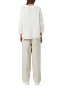 Vitt stickat oversize-tröja med sänkta axlar kombinerad med ljusbeige byxor med vida ben. Slät textur och enkel design.
