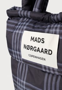Black plaid tote bag with a soft, padded texture. Features a white label with "MADS NØRGAARD COPENHAGEN" printed in bold black letters.
