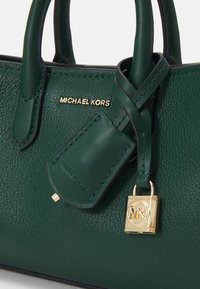 Mørkegrøn tekstureret lædertaske med dobbelte hanke, guldfarvet "Michael Kors" logo, lædermærke og guldfarvet hængelås charm.