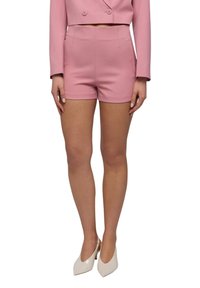 Pantaloni shorts rosa tagliati in modo sartoriale, fatti di un tessuto liscio, con vita alta e tasche laterali. Abbinati a un blazer corto rosa coordinato e tacchi color crema.