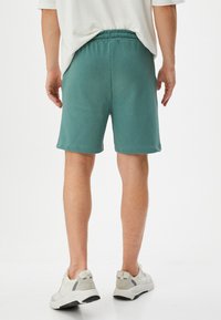 Teal katoenen shorts met een elastische tailleband, een ontspannen pasvorm en zijzakken, gecombineerd met witte sportschoenen.